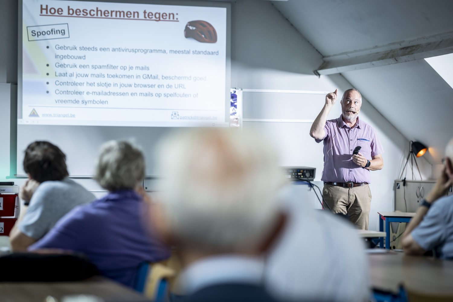 De lesgever geeft uitleg voor het projectiescherm, terwijl de leden in de zaal meekijken.